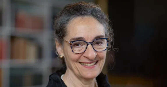 Photo of Dr. Carla Shatz, Professor at Stanford and Director of Bio-X, standing in front of an indistinct background and smiling. She has her short dark hair tied up and is wearing glasses.