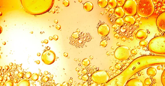 High-contrast photographic image of droplets on a flat surface, some coagulating with each other, in shades of yellow and orange.