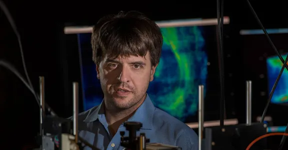 Photo of Dr. Karl Deisseroth in the laboatory, with colorful brain scans in the background.