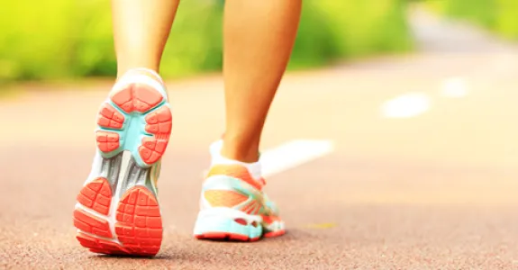 Photo of the feet of a woman wearing athletic sneakers walking down a two-lane path.