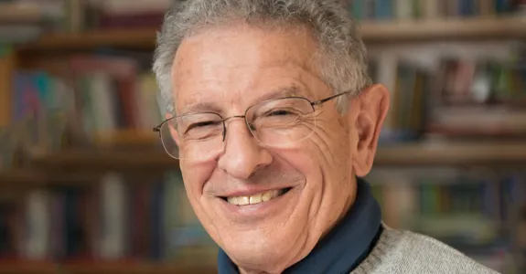 Photo of smiling man in glasses in front of bookshelves.