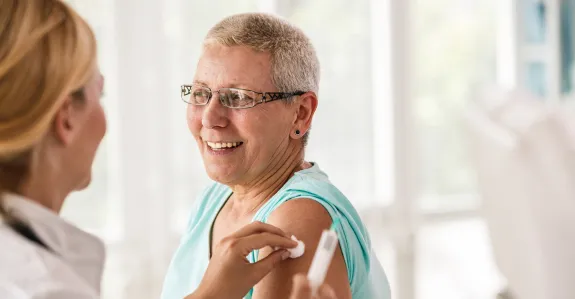 Photo of a female doctor having given an older woman an injection in the upper arm, holding a cotton ball to the site.