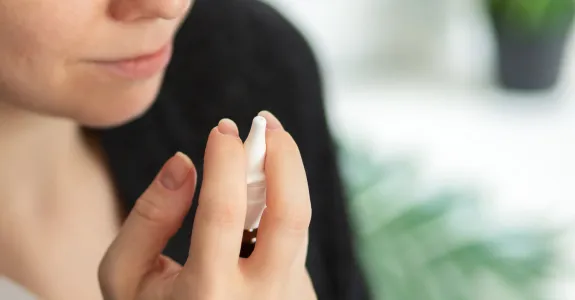 Photo of a woman raising a nasal spray in her hand.