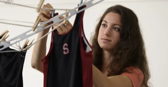 Photo of undergraduate girl hanging Stanford-logo running tops on a rack with clothespins.