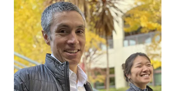 Outdoor photo of Professor KC Huang and postdoc Beverly Fu, both smiling at the camera and wearing Stanford Food branded jackets.