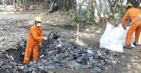 Photo showing two men in orange protective jumpsuits working in a lead waste area, a small pit littered with scraps of metal.