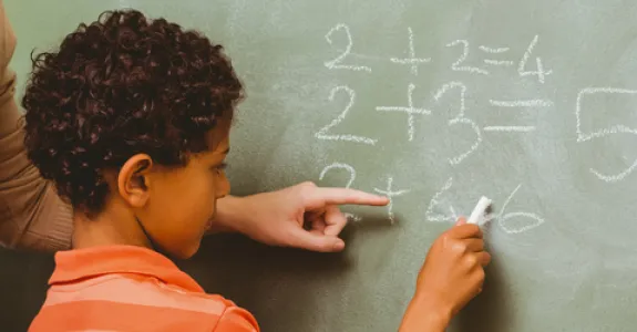 Photo of child doing math problems at chalkboard.