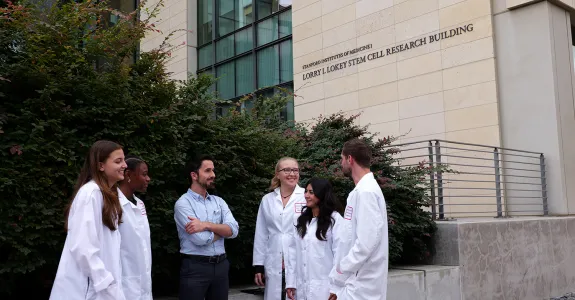 Photo of several researchers standing outside, most of them wearing white lab coats except for male faculty member standing in the middle.