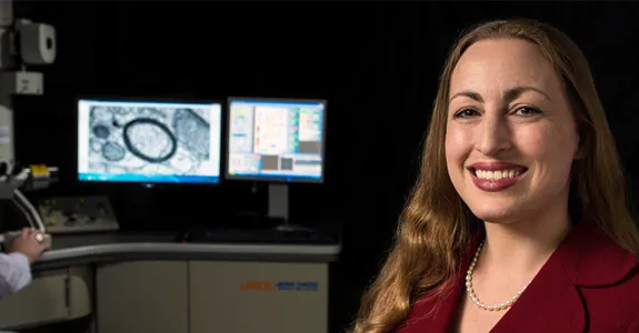 Photo of female PI in laboratory with cell images on screens in background.