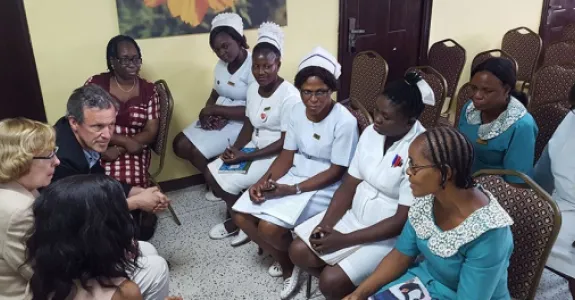 Photo of 3 Stanford faculty seated on left, having a discussion with several Nigerian nurses in uniforms.