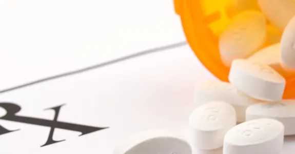 Photo of an orange medication bottle spilling white pills onto a scrip reading "RX".