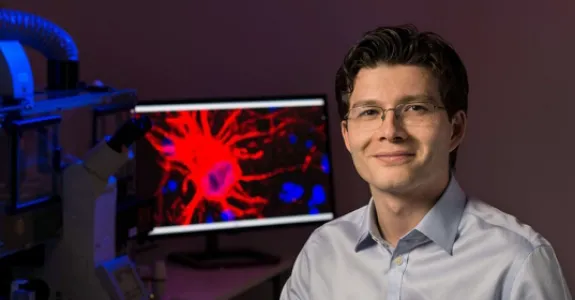 Photo of Dr. Sergiu Pasca in the laboratory, in front of a screen displaying a brain cell.