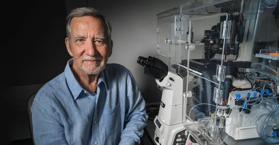 Photo of Professor Jim Spudich sitting in laboratory space next to a complicated microscope apparatus.