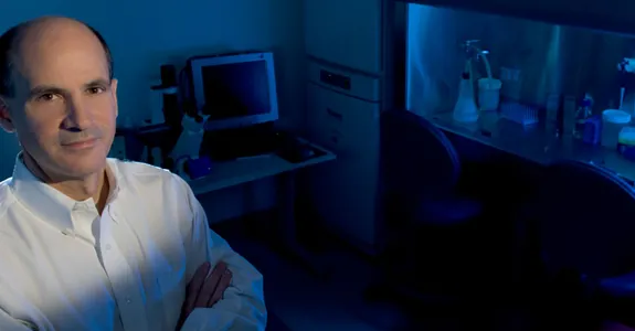 Photo of Dr. Thomas Rando in the laboratory, with fume hood lit up blue in the background.