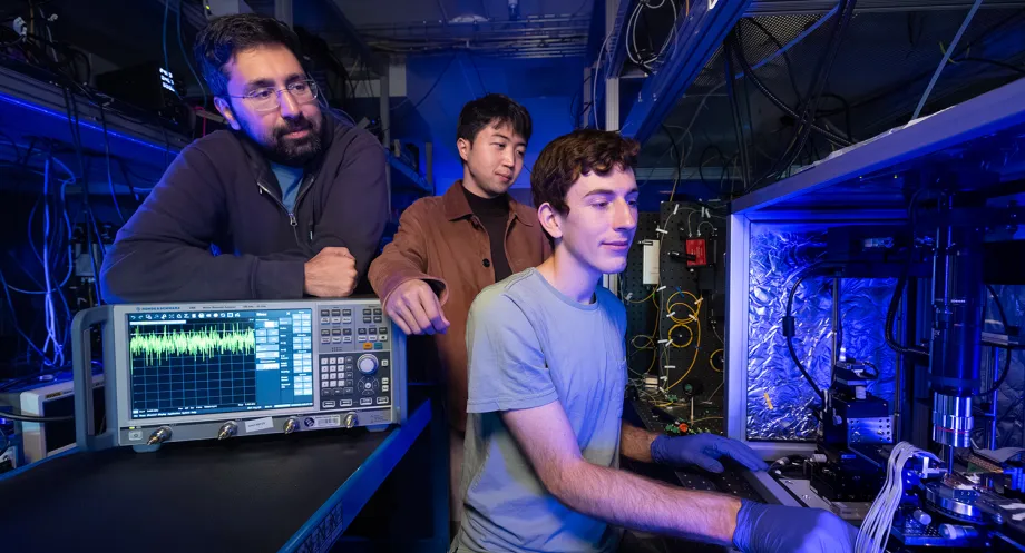 Interior laboratory photo of Stanford doctoral student Devin Dean preparing to measure an optical amplifier chip with Amir Safavi-Naeini and Taewon Park watching over his shoulder.