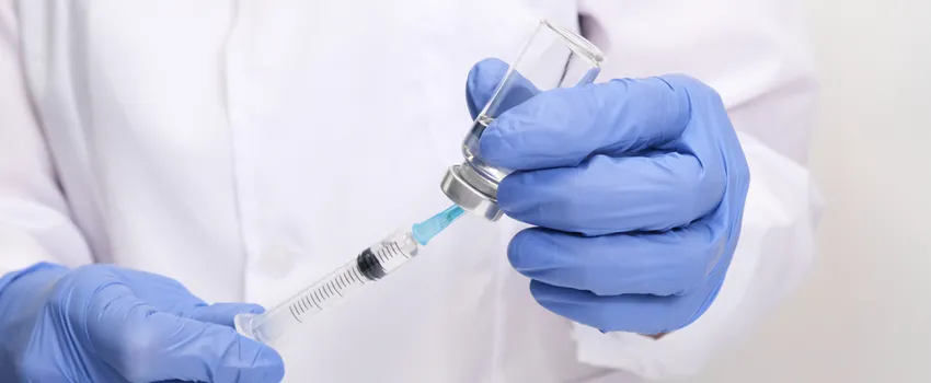 Photo of a scientist's gloved hands holding a syringe with a cap.