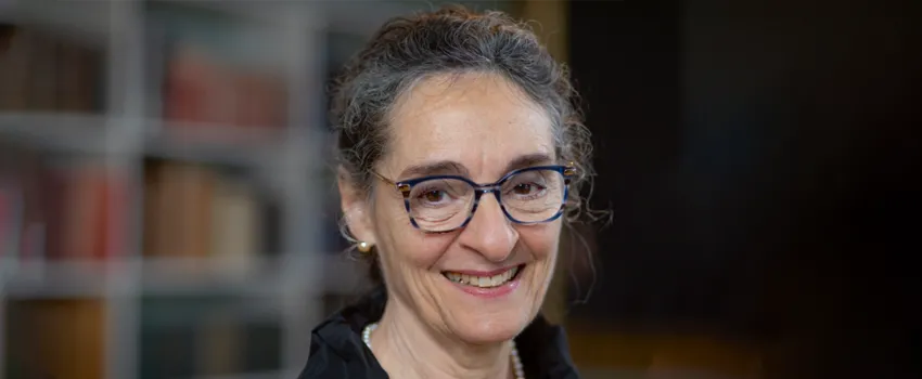 Photo of Dr. Carla Shatz, Professor at Stanford and Director of Bio-X, standing in front of an indistinct background and smiling. She has her short dark hair tied up and is wearing glasses.