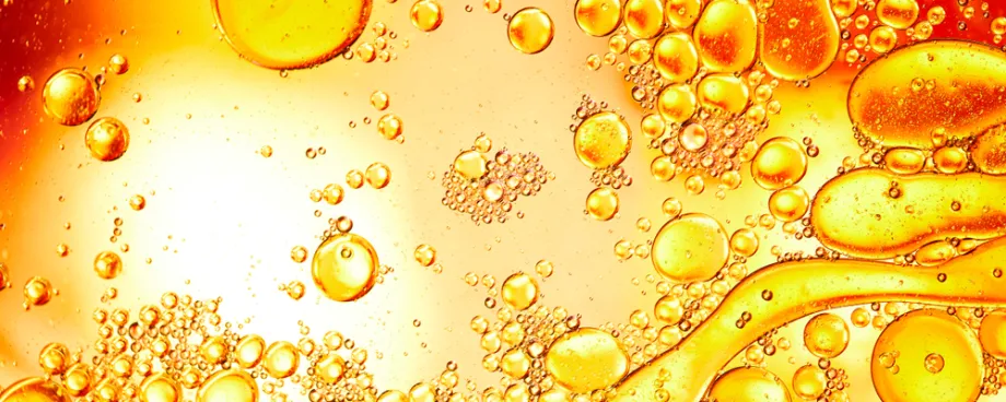 High-contrast photographic image of droplets on a flat surface, some coagulating with each other, in shades of yellow and orange.