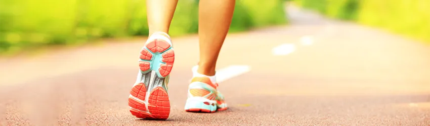 Photo of the feet of a woman wearing athletic sneakers walking down a two-lane path.