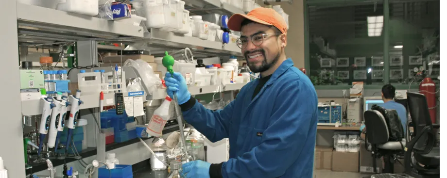 Photo of young Latino male graduate student holding lab equipment in front of a laboratory bench.