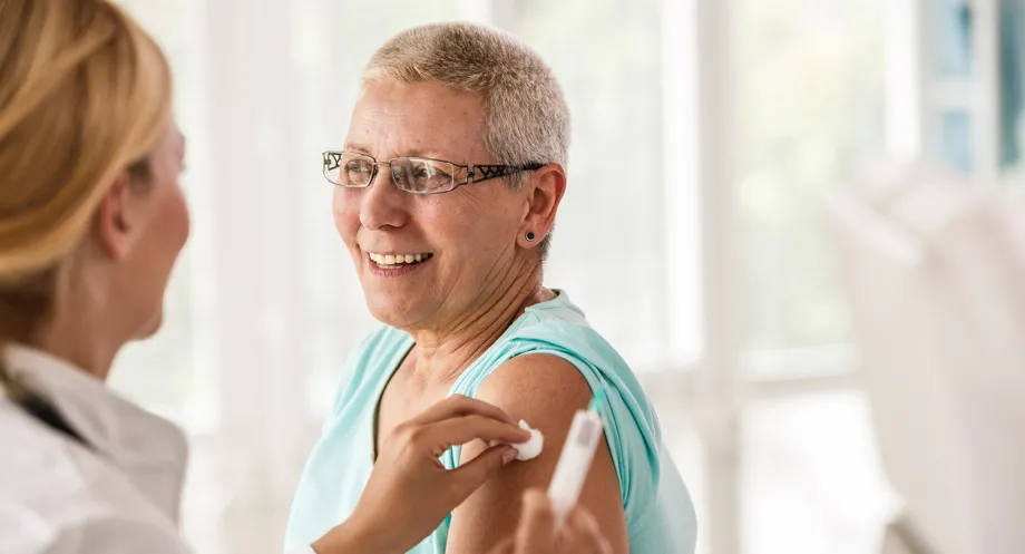 Photo of a female doctor having given an older woman an injection in the upper arm, holding a cotton ball to the site.