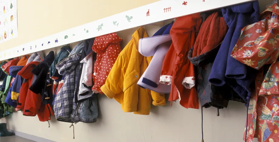 Photo of colorful children’s coats hung up on a wall rack.