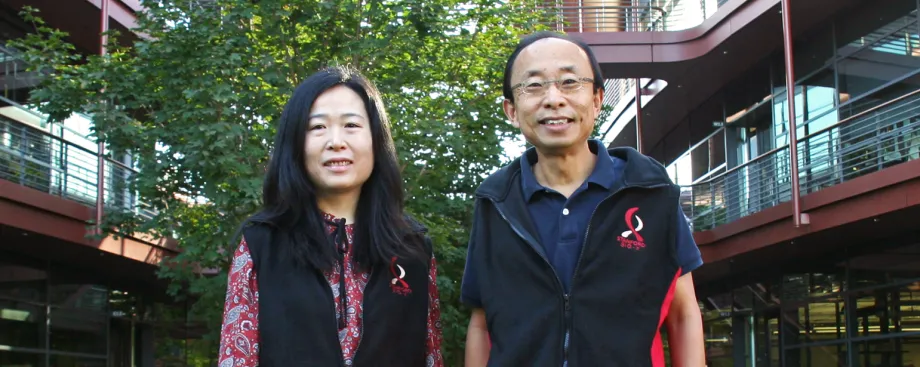 Outdoor photo of an Asian female faculty member and Asian male faculty member smiling at the camera outside of the Clark Center, wearing matching fleece vests with the Bio-X logo.