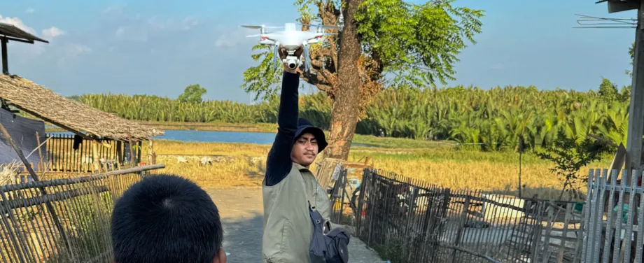 A local drone pilot, Muh. Yusuf Fadhel Marwiji, in Makassar, Indonesia, prepares to launch a drone to search for discarded tires that collect rainwater and become mosquito breeding sites, as a curious child watches