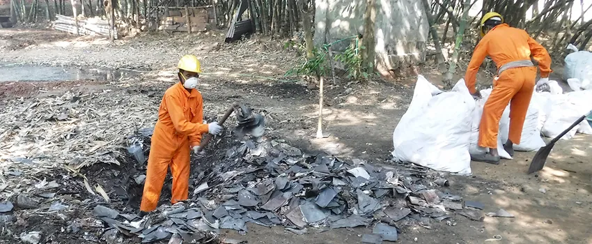 Photo showing two men in orange protective jumpsuits working in a lead waste area, a small pit littered with scraps of metal.