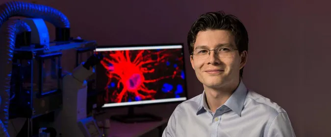 Photo of Dr. Sergiu Pasca in the laboratory, in front of a screen displaying a brain cell.