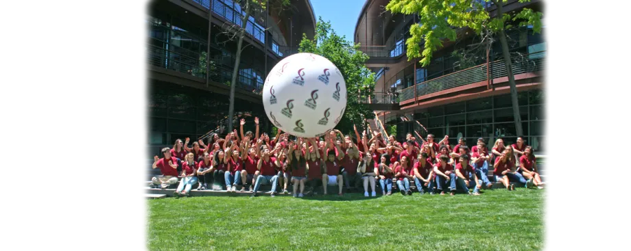 Group photo of 65 undergraduates seated, wearing red shirts and rolling a large white ball with Bio-X logos across the group's raised hands.