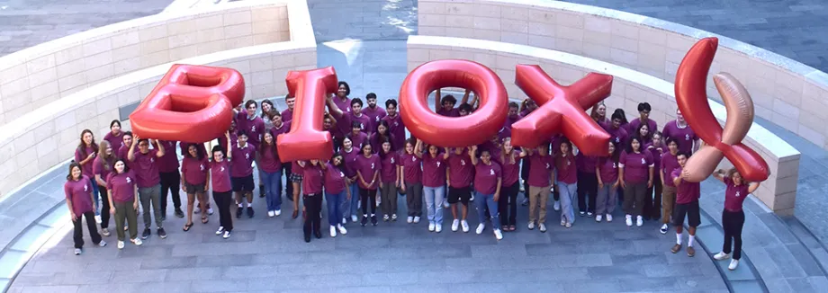 Outdoor photo of 76 students wearing matching red shirts and holding up inflated letters reading "Bio X"