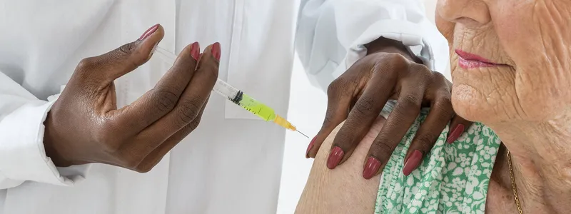 Photo of an older woman receiving a vaccination injection in the shoulder.