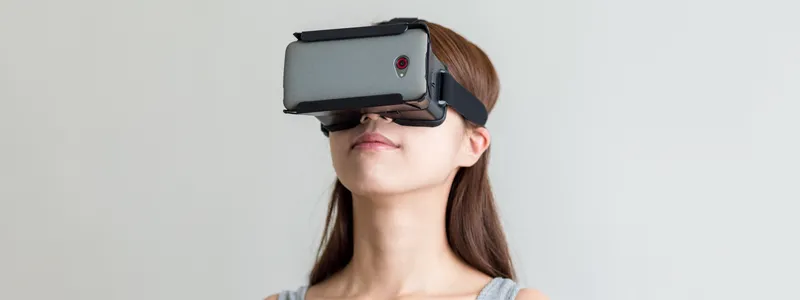 Photo of a woman wearing a virtual reality headset in front of a gray background.
