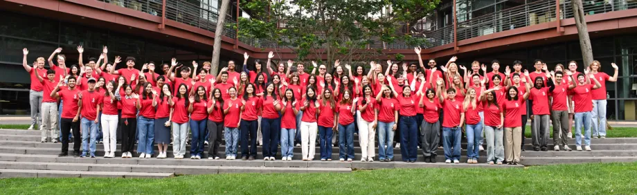 Outdoor photo of 86 undergraduates in matching shirts, waving.