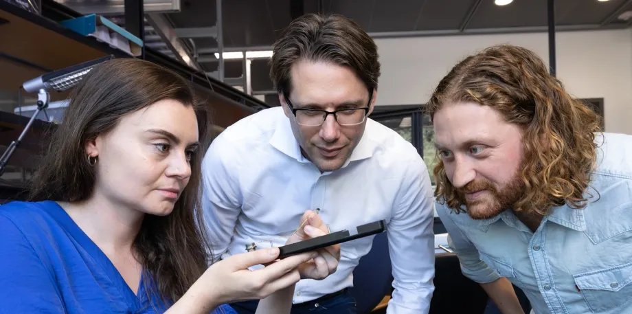 Photo of faculty member and two researchers looking at a device in the lab.