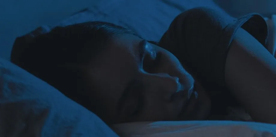 Dark blue tinted photo of a woman's head resting on a pillow as she sleeps.