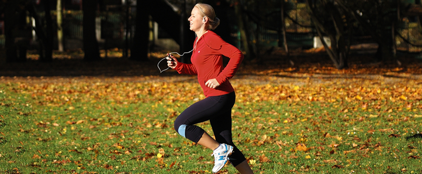 Photo of a young blonde woman running across a field with fallen leaves.