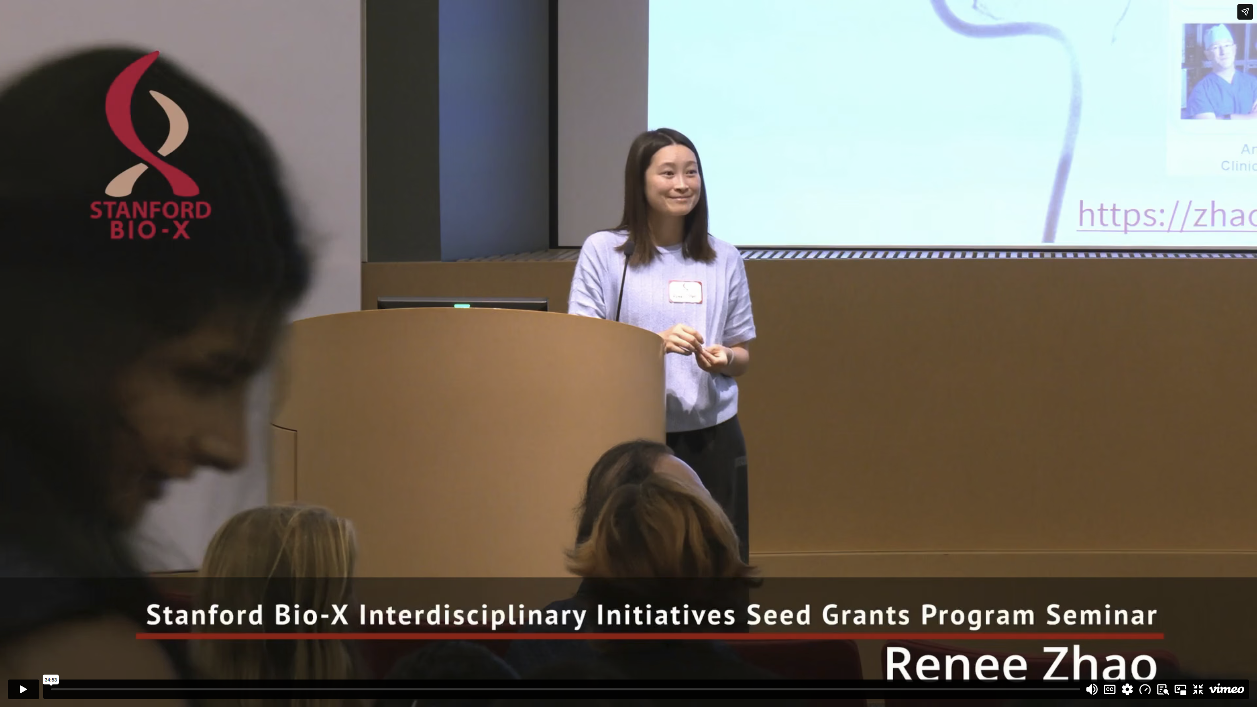 Video thumbnail showing faculty member standing at the front of an auditorium.