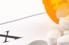 Photo of an orange medication bottle spilling white pills onto a scrip reading "RX".