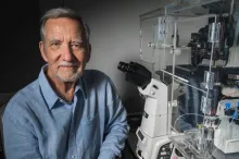 Photo of Professor Jim Spudich sitting in laboratory space next to a complicated microscope apparatus.