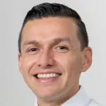 Photo of a smiling Latino man with short dark hair, Dr. Andres Carenas, Assistant Professor of Epidemiology and Population Health at Stanford University.